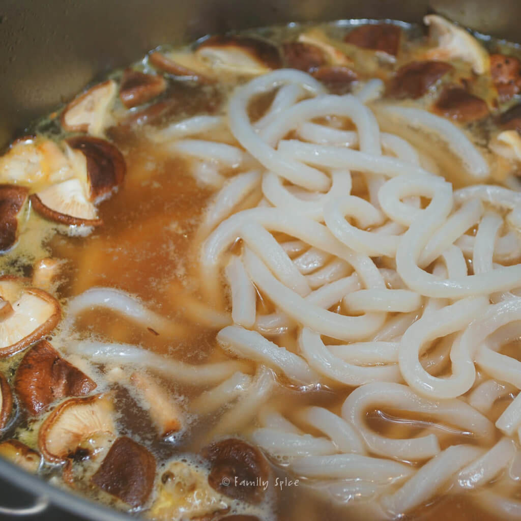 Adding udon noodles to a pot of soup with mushrooms