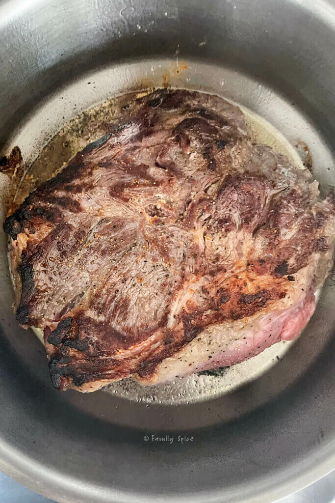 Top view of a stainless pot with a browned chuck roast in it