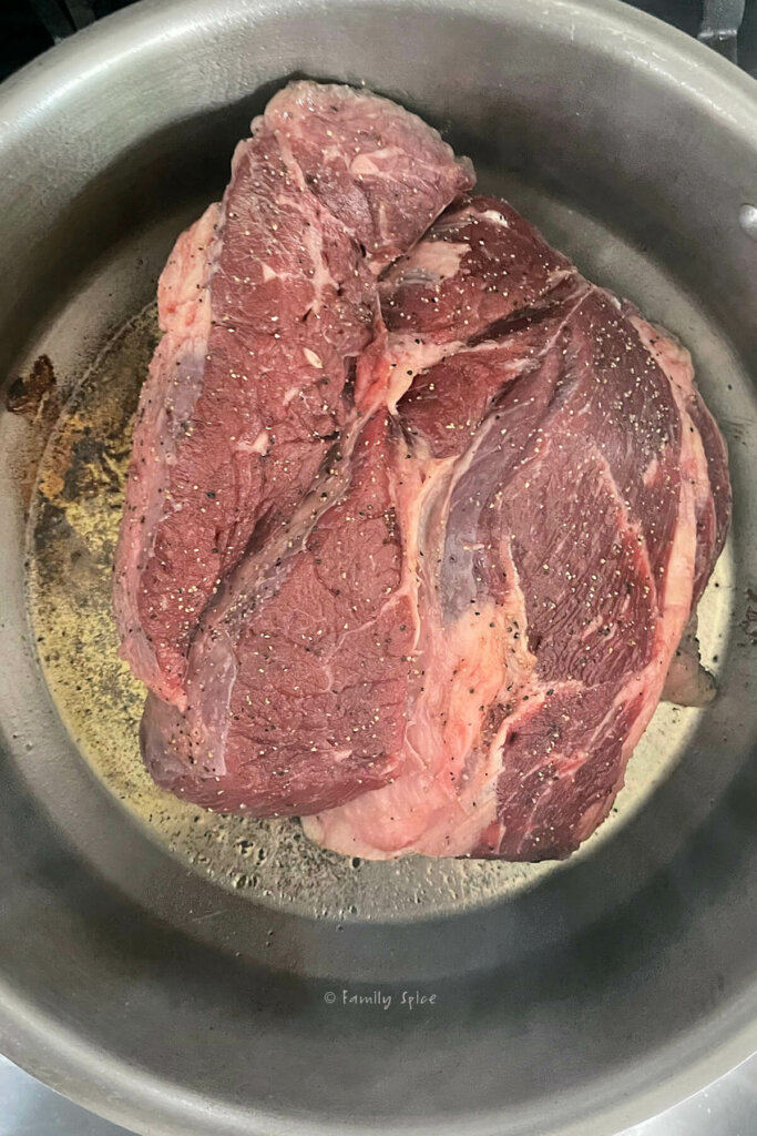 Top view of a stainless pot with a raw chuck roast browning in it
