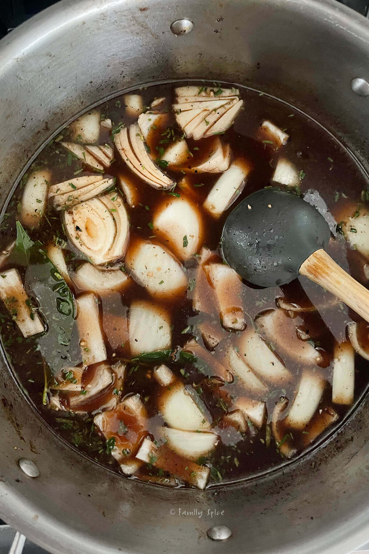 A stainless pot with onion slices and herbs in a beef broth