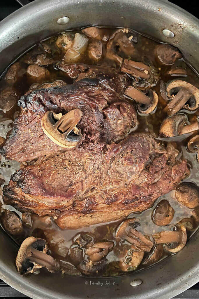 Top view of a stainless pot with a braised chuck roast with mushrooms in it