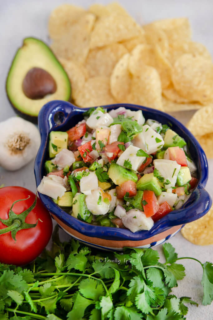 Mexican ceviche in a blue terracotta bowl with tortilla chips and ingredients around it