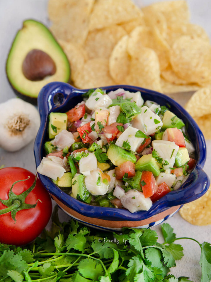 Mexican ceviche in a blue terracotta bowl with tortilla chips and ingredients around it
