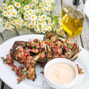 A white plate with a chile lime grilled artichoke garnished with pico de gallo and served with a chile mayo.