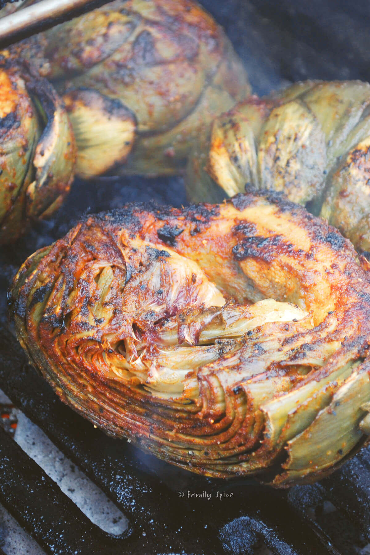 Halved artichokes seasoned with chile lime and cooking on a grill