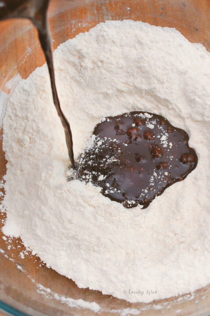 Pouring melted chocolate mixture into dry ingredients in a mixing bowl to make chocolate root beer cake