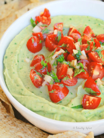 Closeup of avocado hummus in a white bowl and garnished with chopped tomatoes