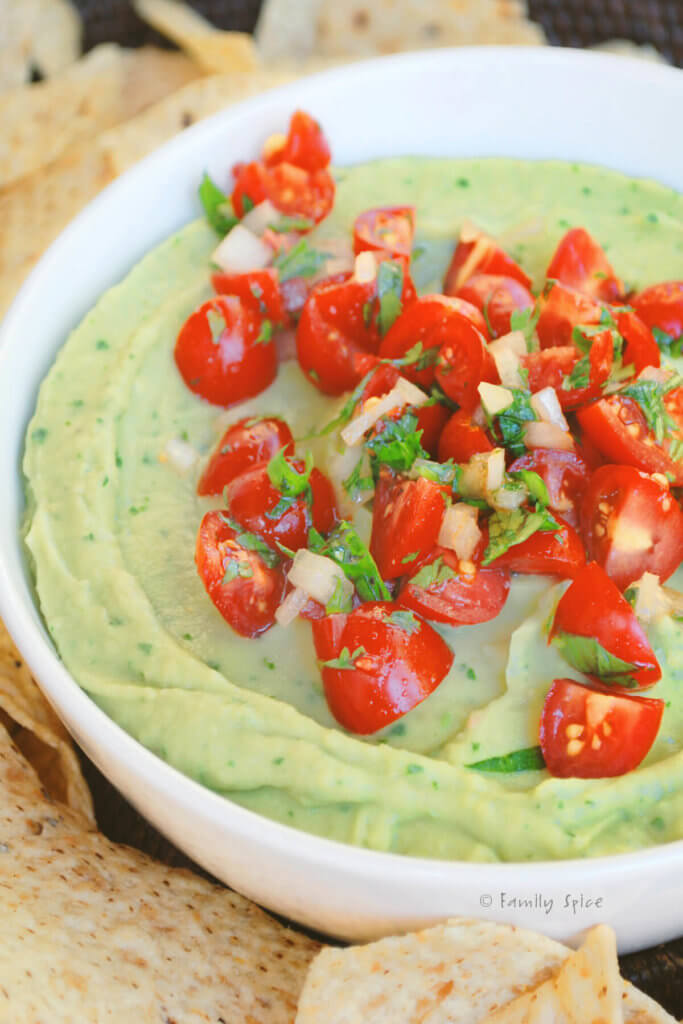 Avocado hummus in a white bowl and garnished with chopped tomatoes
