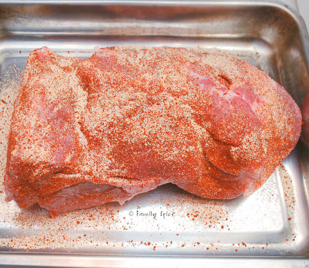 A pork shoulder roast seasoned and in a roasting pan