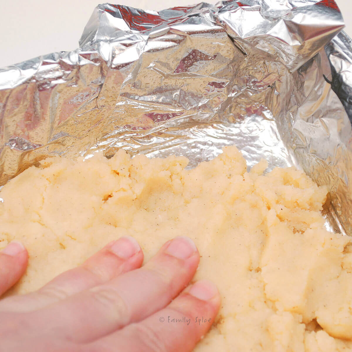 A hand pressing shortbread dough into a foil lined pan