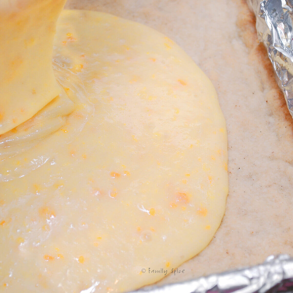 Pouring kumquat filling over shortbread crust in a foil lined baking pan