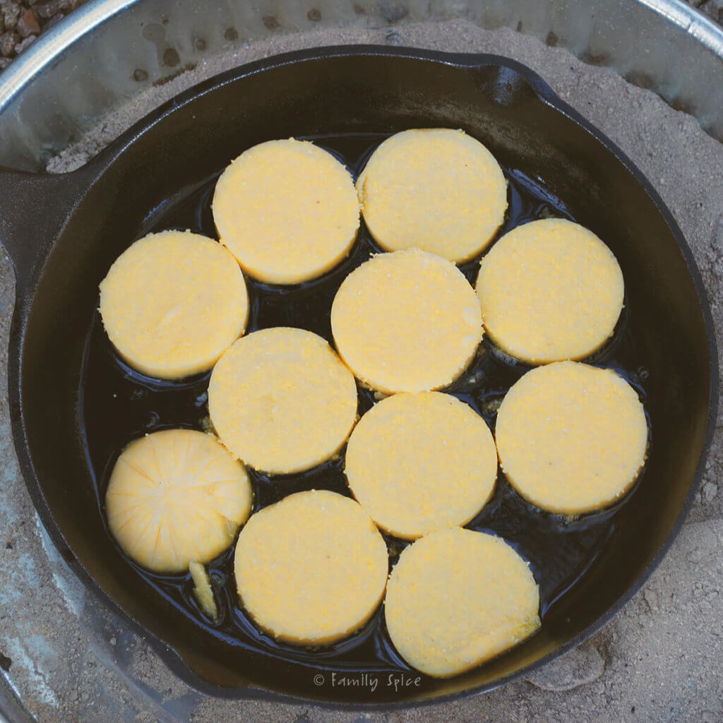 frying polenta rounds in a cast iron pan over hot coals
