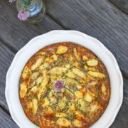 Top view of a fingerling potato kookoo in a ceramic pie dish on a wood background with chive blossoms next to it
