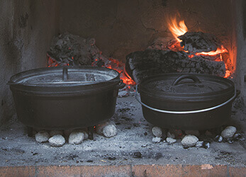 two dutch ovens in an outdoor fireplace with hot coals