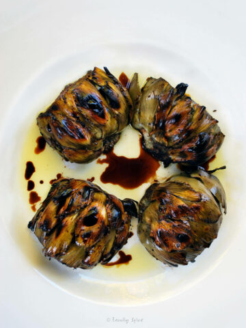 Top view of grilled artichokes on a white plate with balsamic vinegar and olive oil