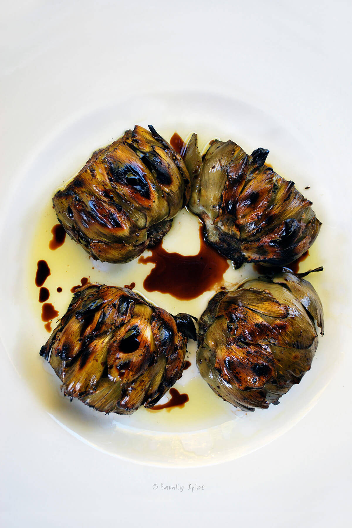 Top view of grilled artichokes on a white plate with balsamic vinegar and olive oil