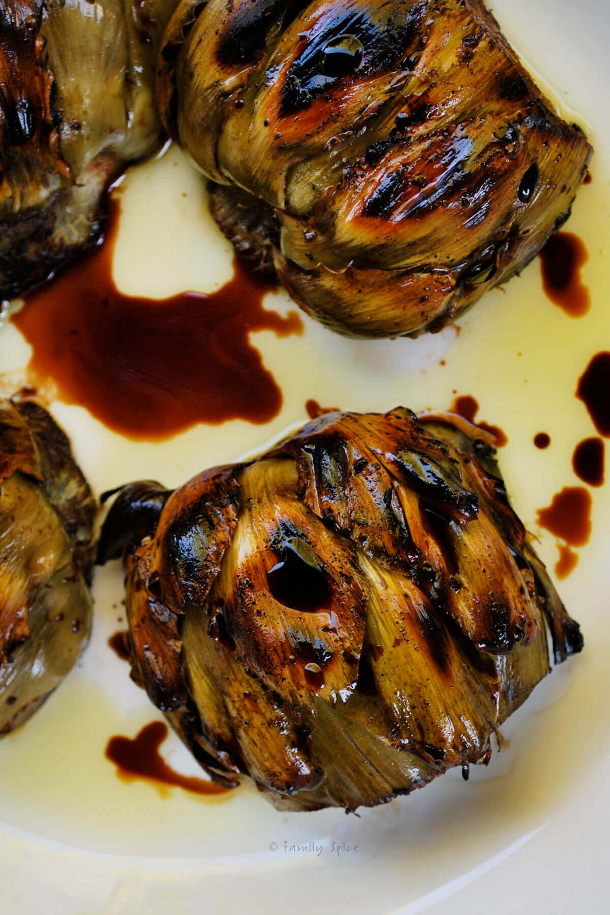 Top view closeup of grilled artichokes on a white plate with balsamic vinegar and olive oil