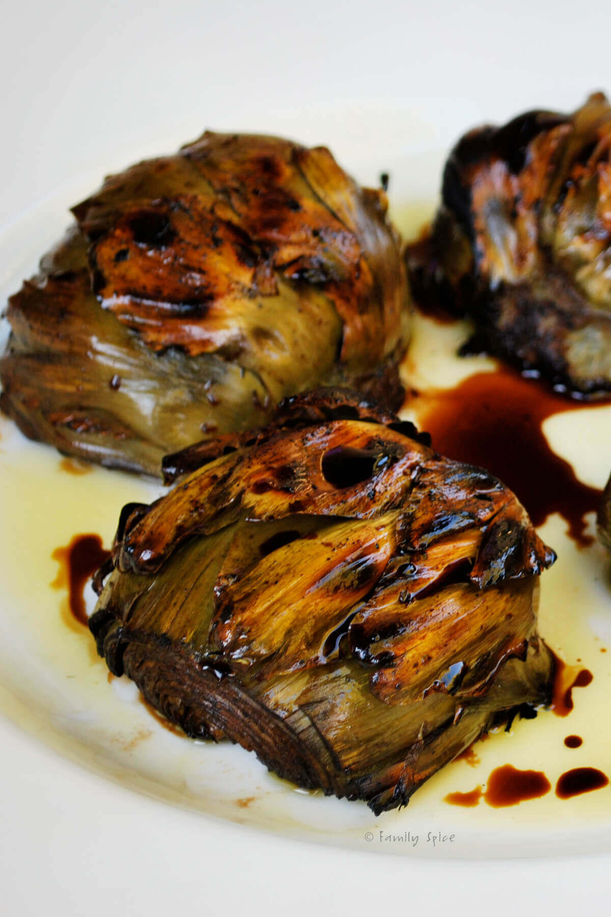 Side view closeup of grilled artichokes on a white plate with balsamic vinegar and olive oil