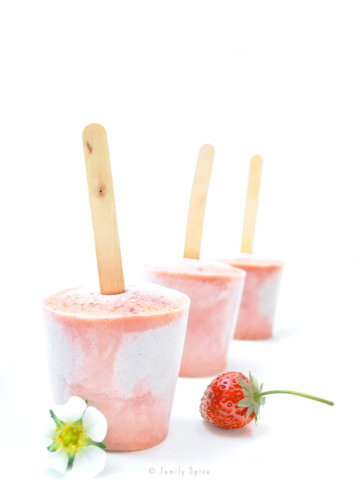 Three pink strawberry smoothie popsicles with a strawberry on a white background