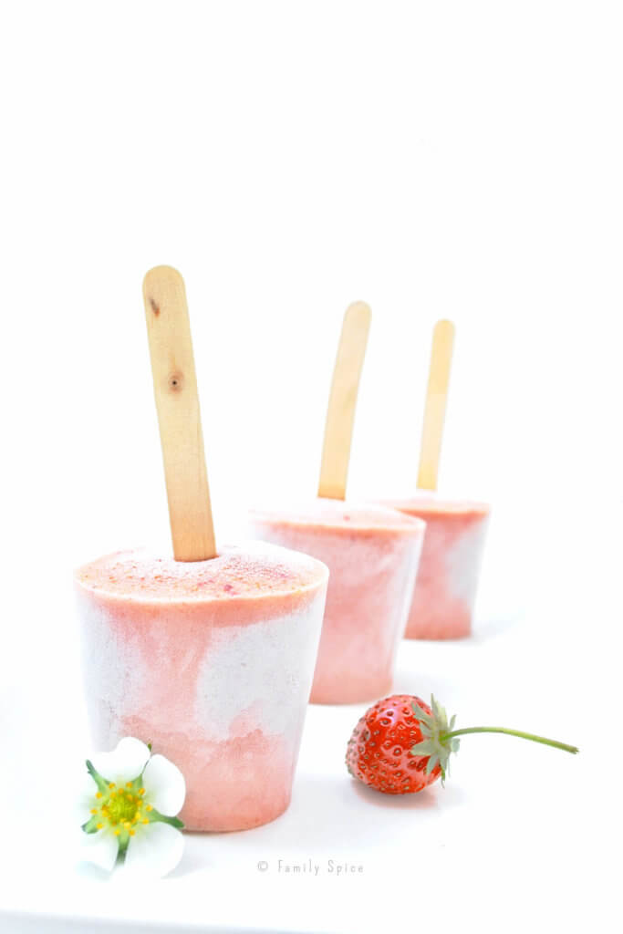 Three pink strawberry smoothie popsicles with a strawberry on a white background