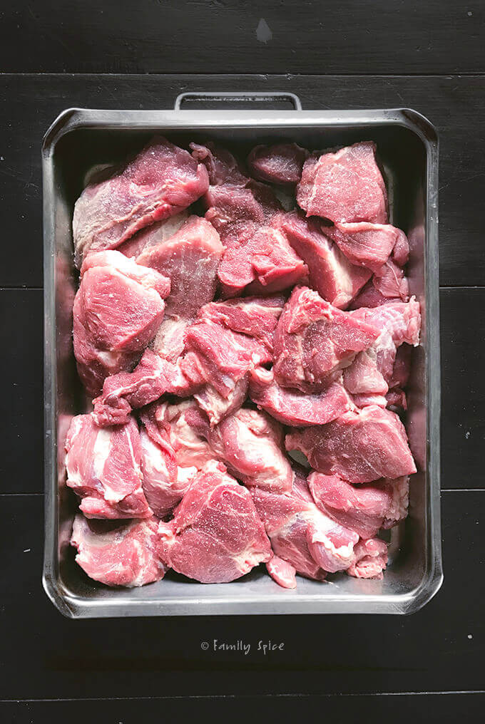 A pork shoulder roast cut into large chunks in a roasting pan by FamilySpice.com