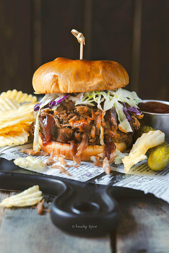 A stuffed pulled pork sandwich with coleslaw, chips and pickles by FamilySpice.com