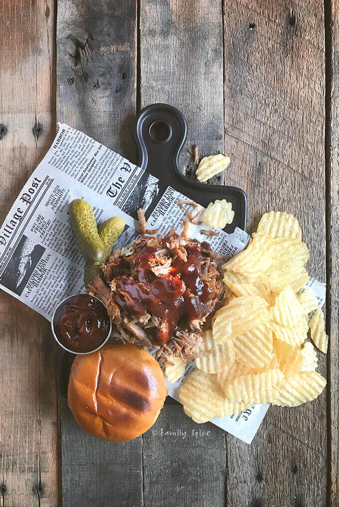 Top view of an open pulled pork sandwich with barbecue sauce and served with chips and pickles by FamilySpice.com