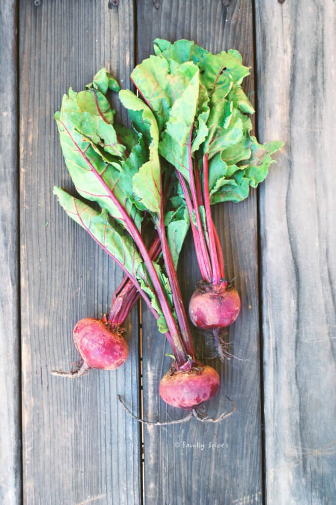 3 fresh beets with greens attached on a wood table