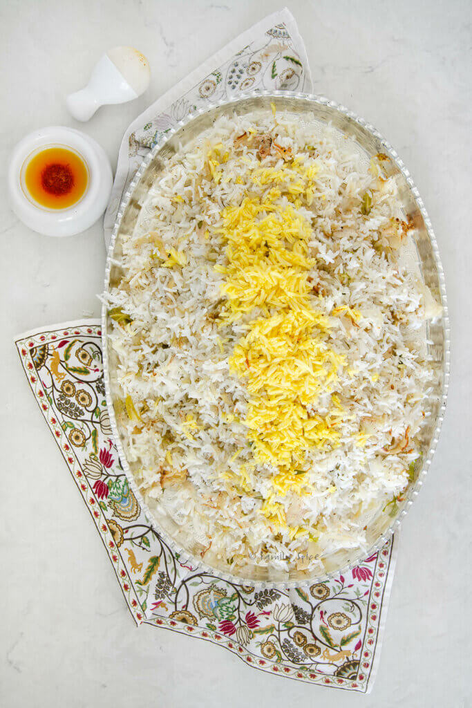 Top view of cabbage rice (kalam polo) with saffron on top on a silver oval platter with a mortal and pestle with saffron liquid spoon next to it
