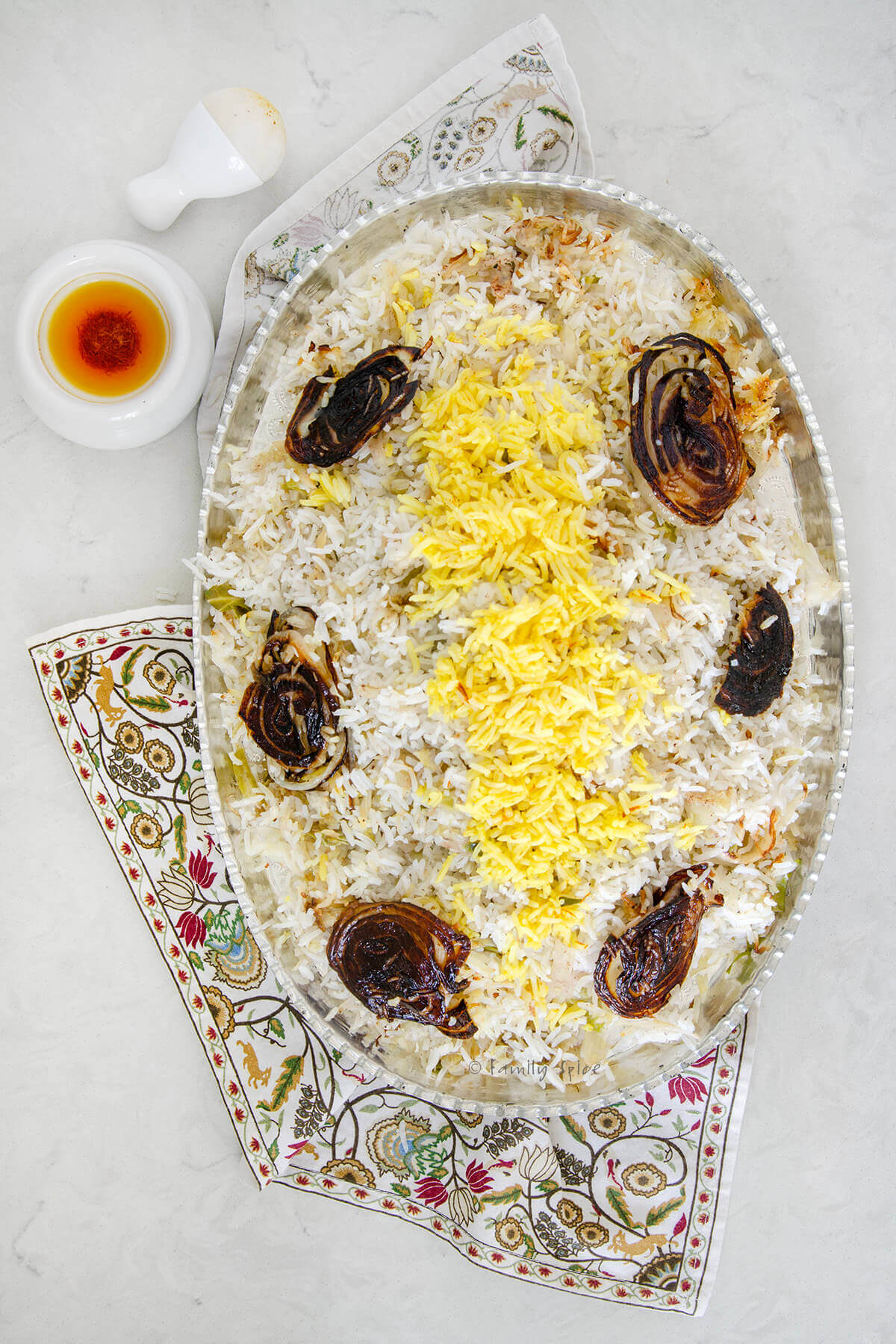 Top view of cabbage rice (kalam polo) with onion tadigh on a silver oval platter with a mortal and pestle with saffron liquid spoon next to it