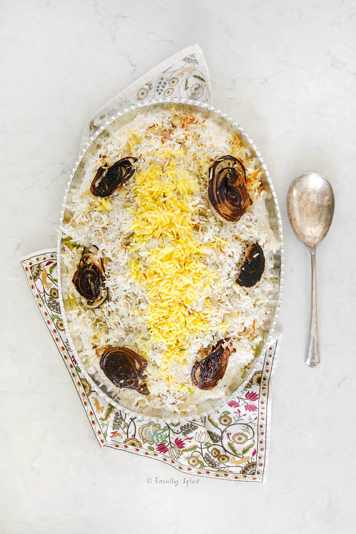 Top view of cabbage rice (kalam polo) with onion tadigh on a silver oval platter with a serving spoon next to it