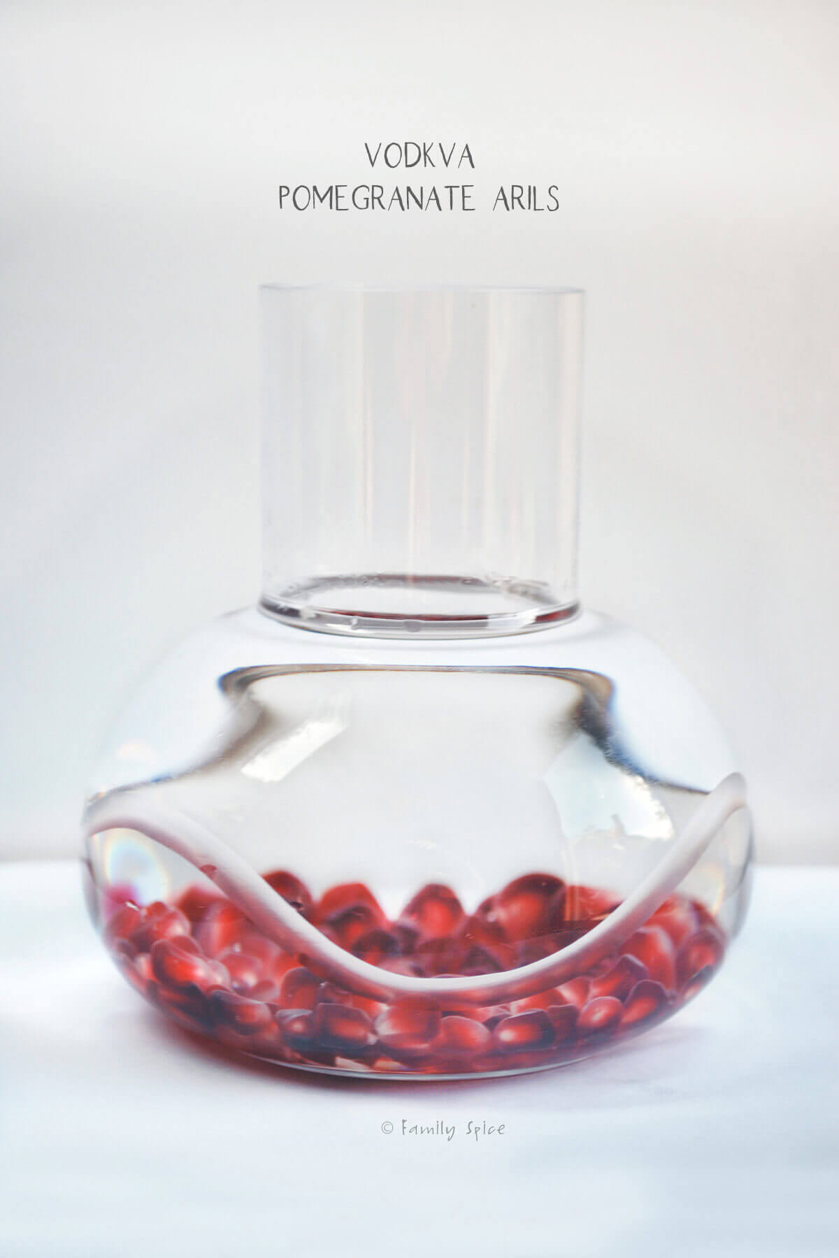Side view of pomegranate arils in a bottle of vodka with ingredients listed