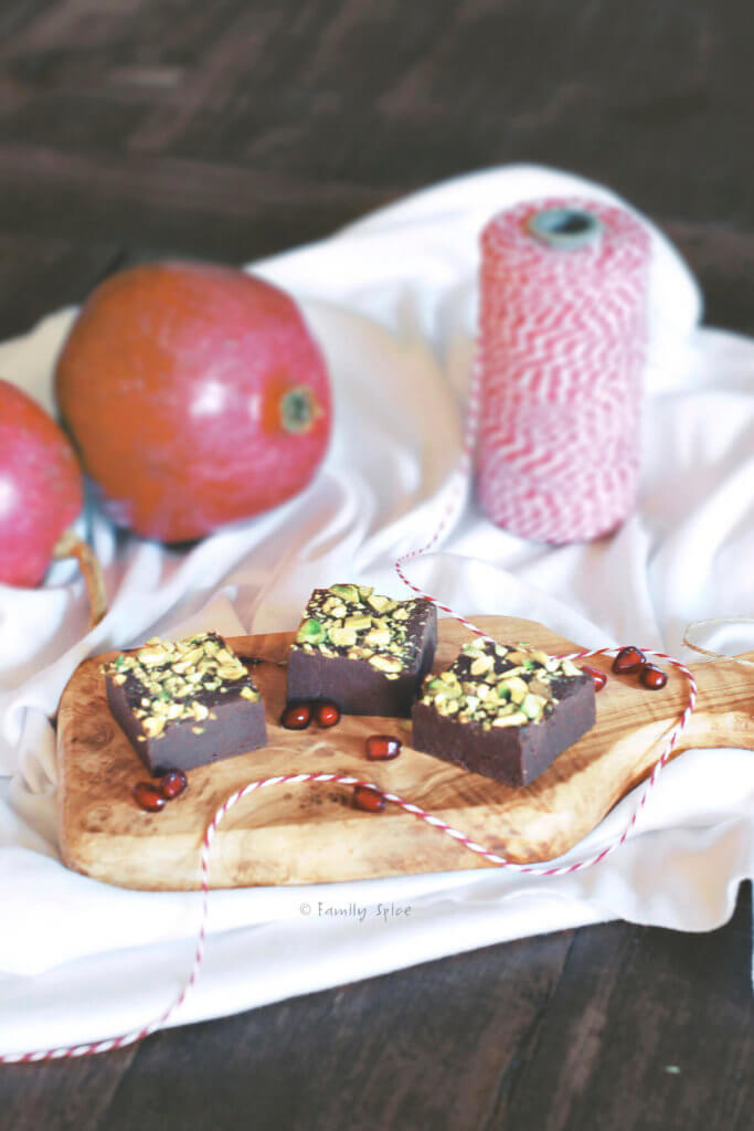3 pieces of pomegranate fudge topped with pistachios with pomegranates behind it