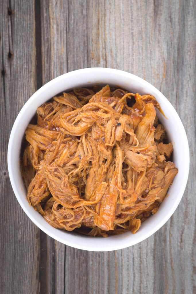 Shredded orange pulled pork in a white bowl on a wooden surface