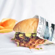 orange bbq pulled pork sandwich wrapped in newspaper with orange peels behind it