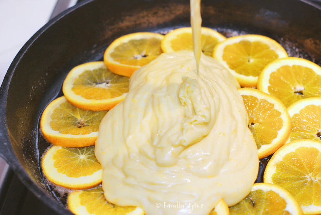 Orange cake batter being poured over cast iron pan lined with orange slices