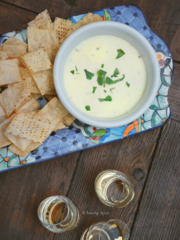 Top view of a bowl of queso in a decorated rectangular platter with tortilla chips and shot glasses with tequila