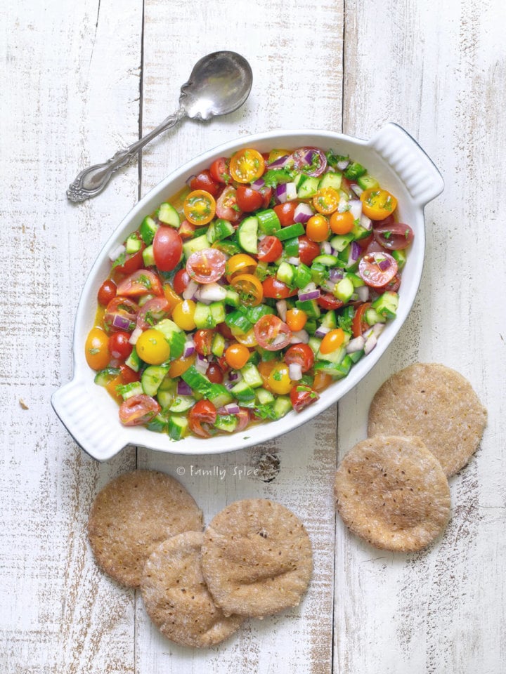 An oval dish with shirazi salad, cucumber tomato salad, with pita rounds next to it