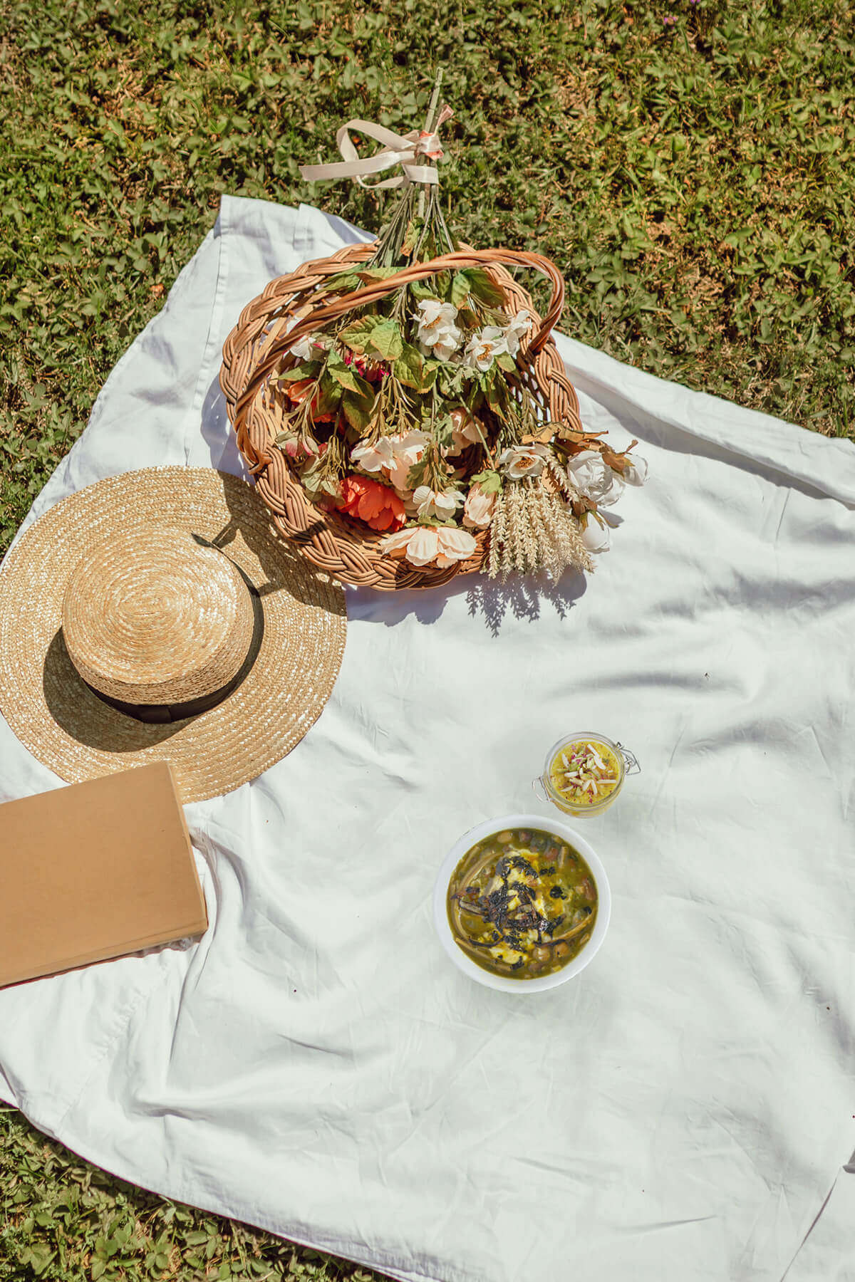 Top view of a picnic blanket with a straw hat, flowers and foods eaten for sizdah bidar