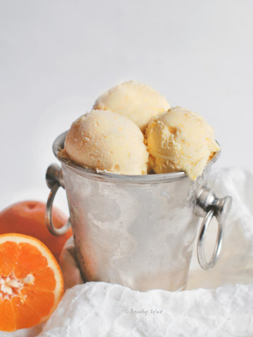 Scoops of orange sherbet in a small metal ice bucket with orange halves