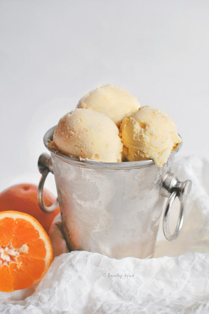 Scoops of orange sherbet in a small metal ice bucket with orange halves