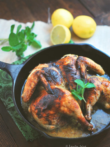 A cast iron pan with a roasted spatchcocked chicken, lemons and herbs