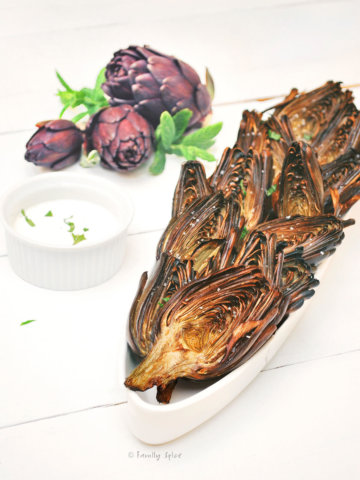 A thin oval serving platter with baby purple artichokes