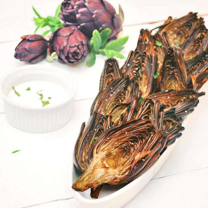A thin oval serving platter with baby purple artichokes