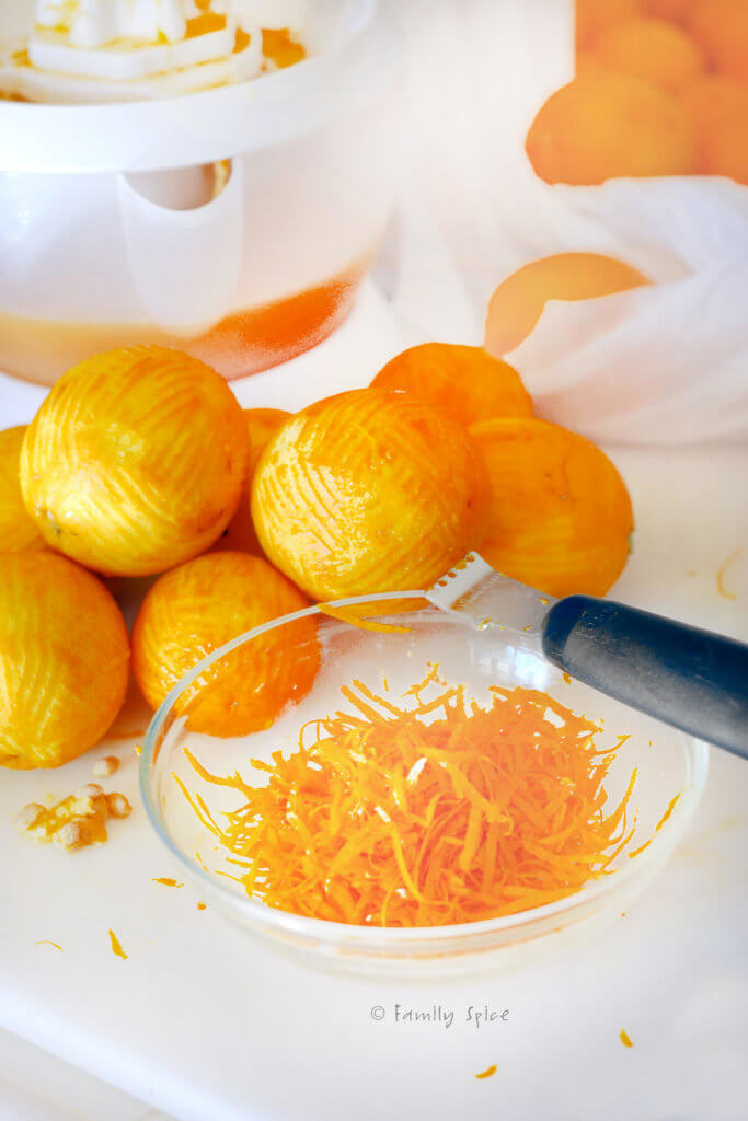 A bowl of orange zest with a zester and zested oranges behind it