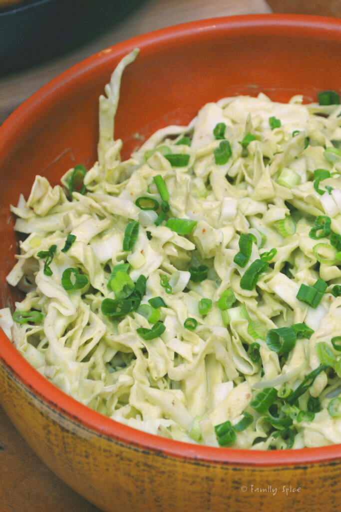 A rustic bowl of creamy avocado cole slaw garnished with green onions