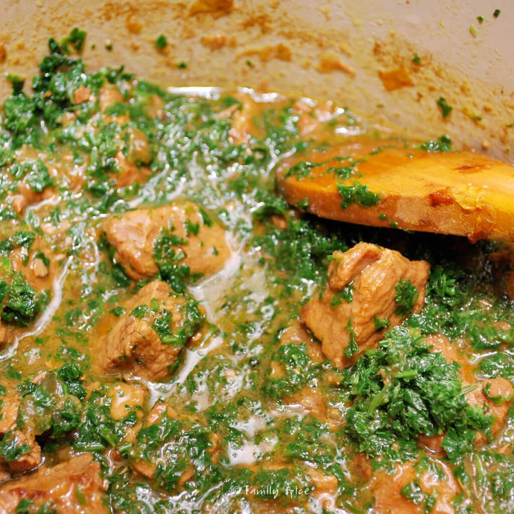 Adding chopped herbs to stew mixture to make khoresh chaghaleh badoom
