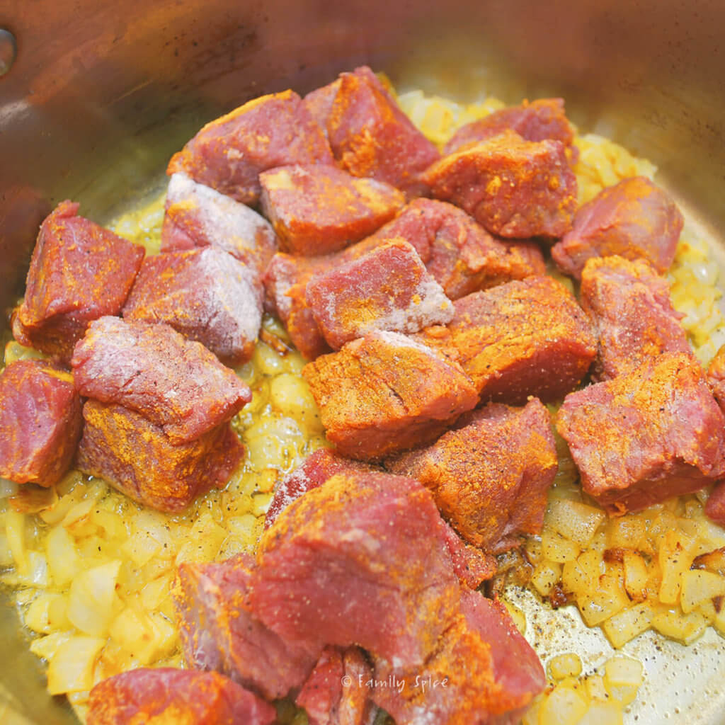 Adding cubes of beef stew meat to turmeric colored sautéed chopped onions in a pot