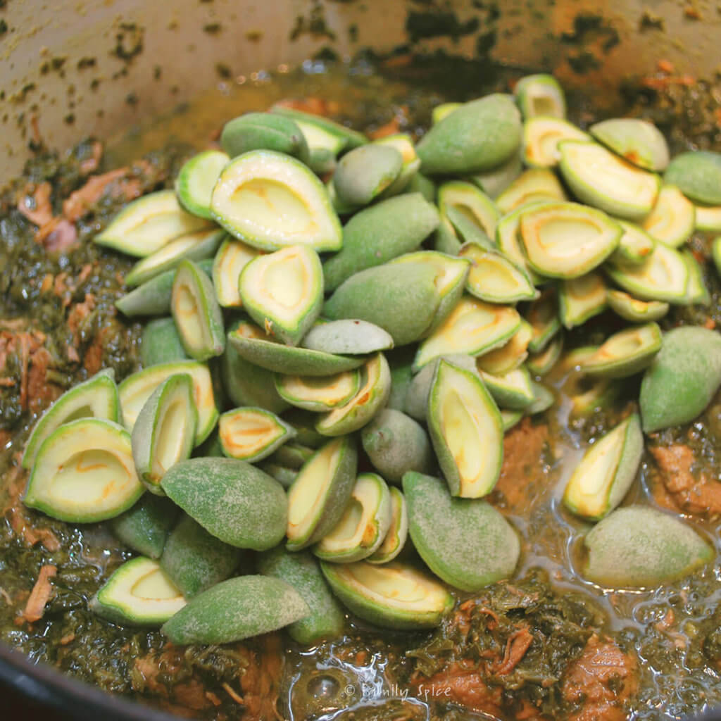 Adding halved green almonds to herb stew mixture to make khoresh chaghaleh badoom