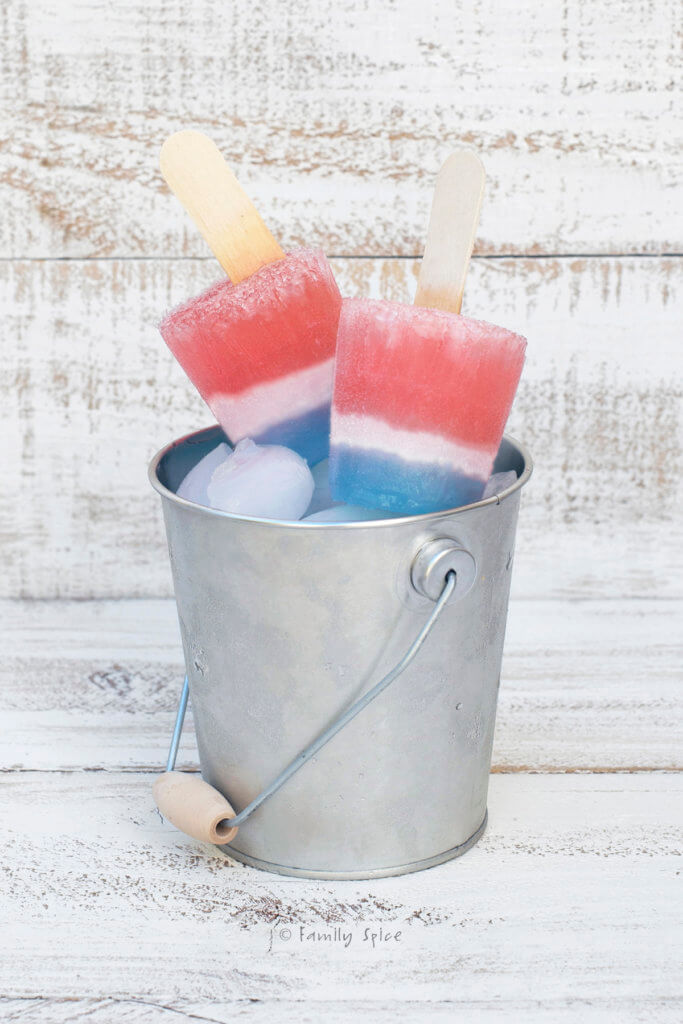Two red, white and blue popsicles sitting in a small bucket of ice